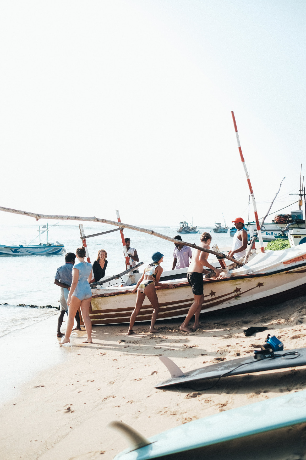 Guests and local fishermen pushing an outrigger boat off the sand