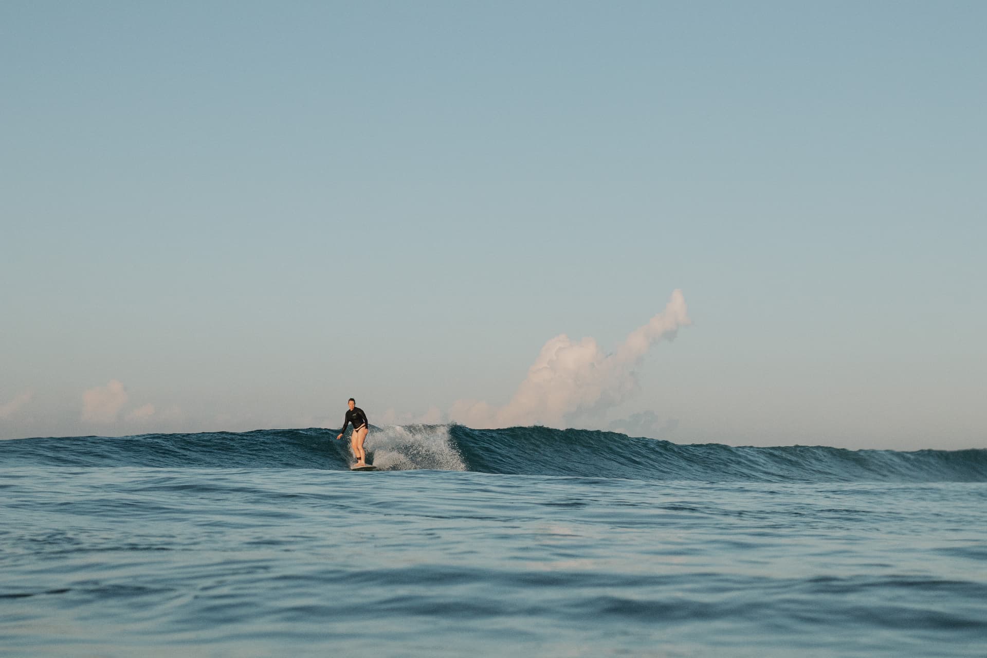 A surfer riding an open green wave under a soft sky