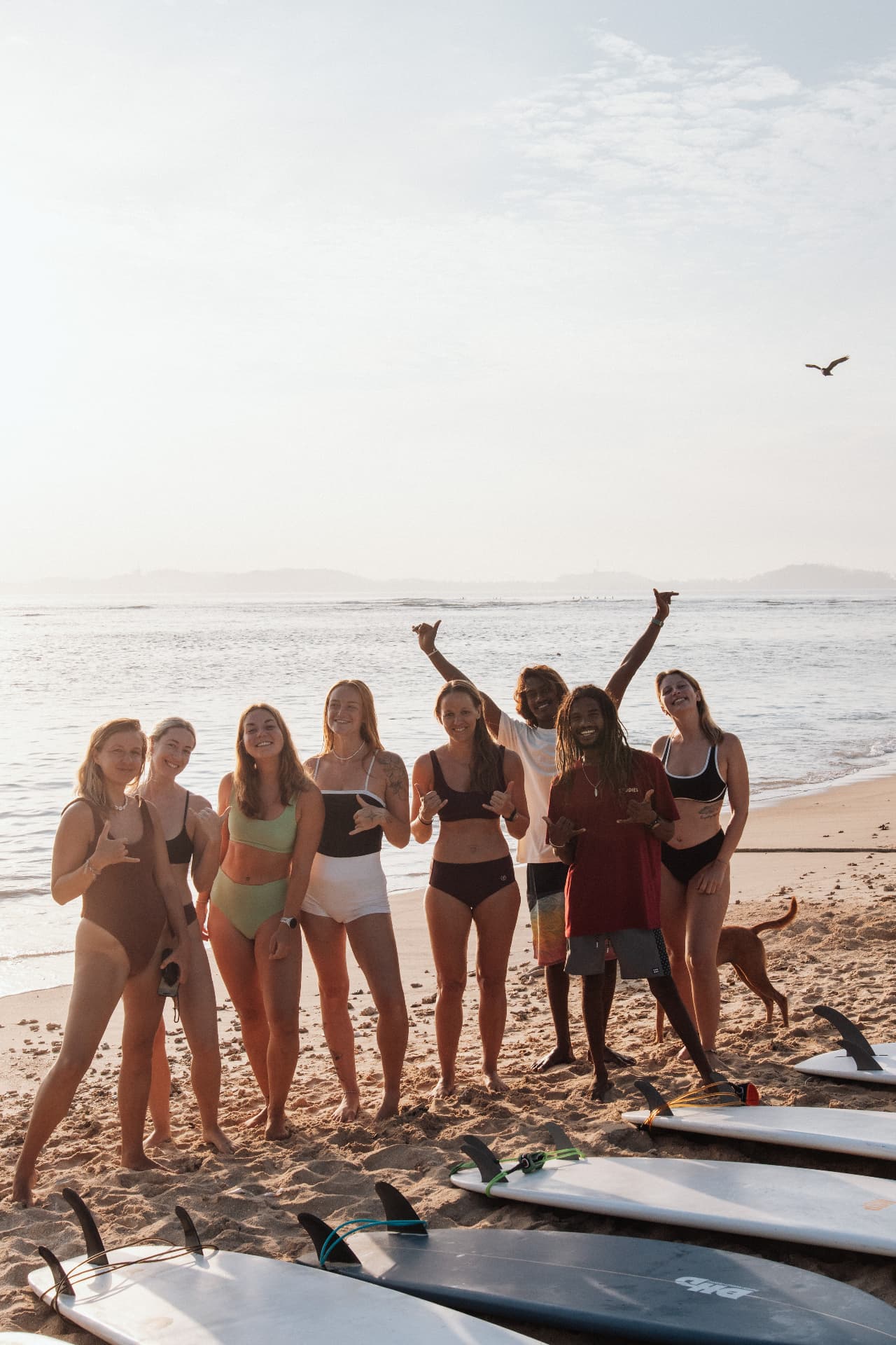 A group of guests and instructors posing on the beach with surfboards
