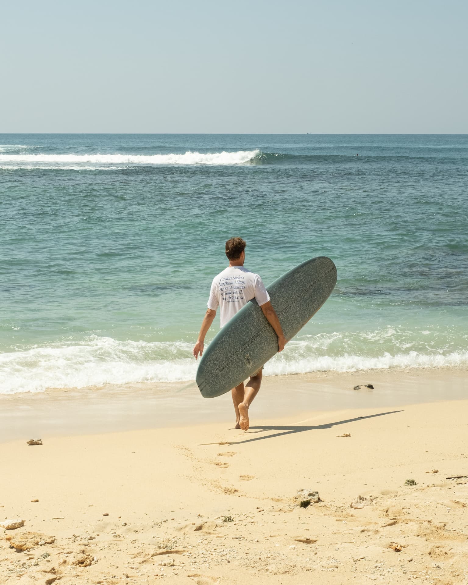 A surfer walking down the sand toward the waves