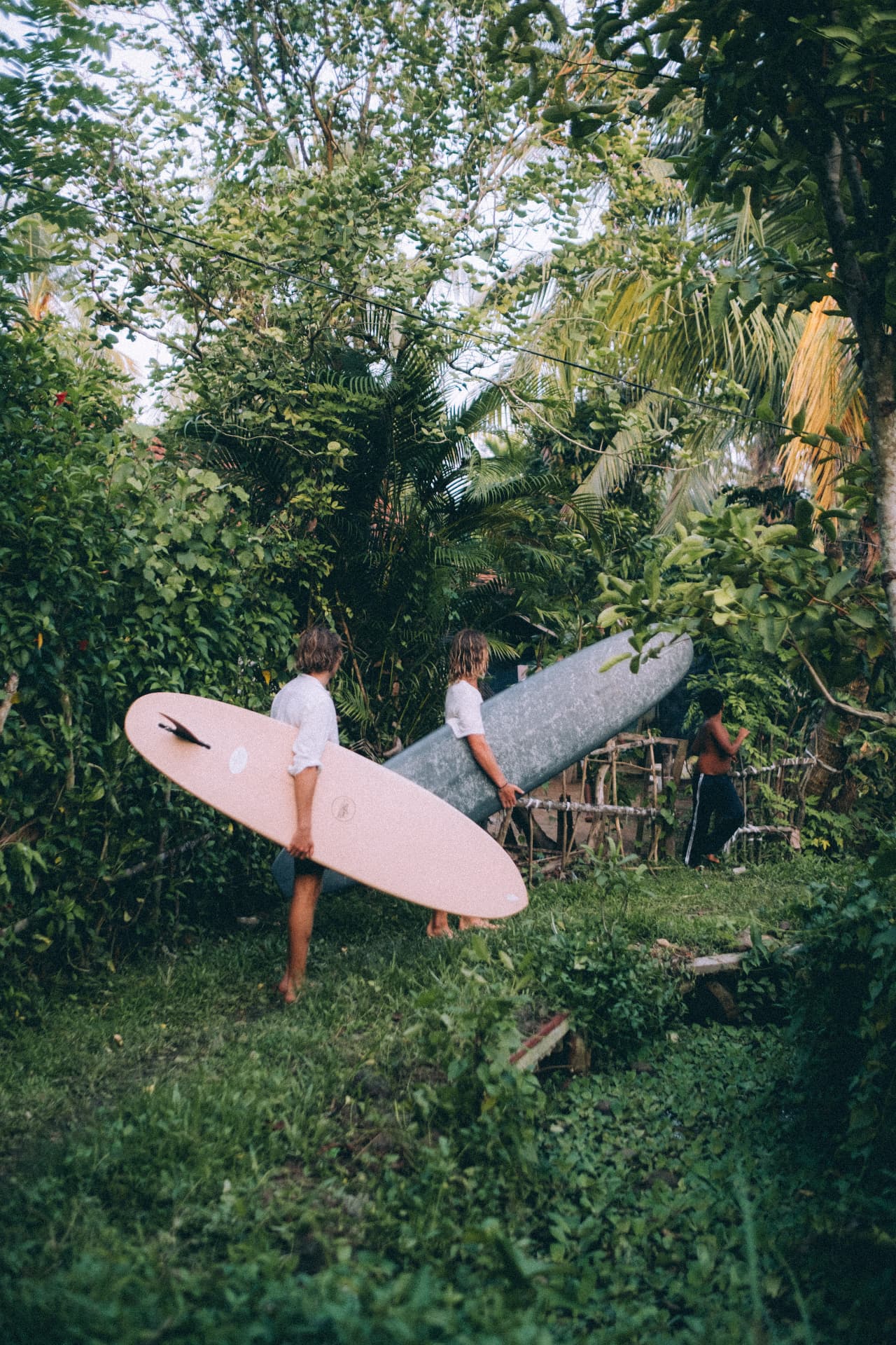 Two guests carrying longboards through the villa garden
