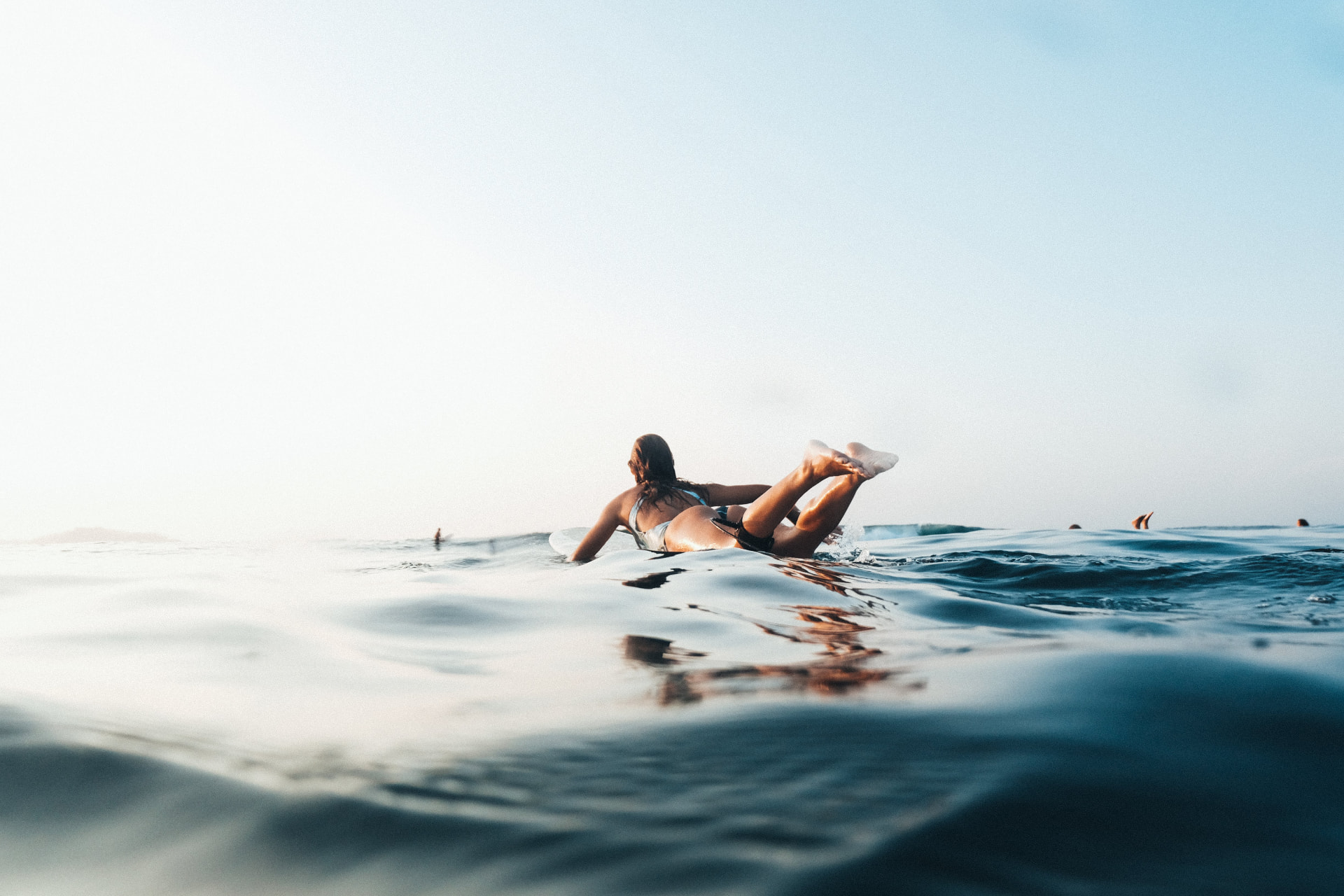 A surfer paddling out over glassy morning water