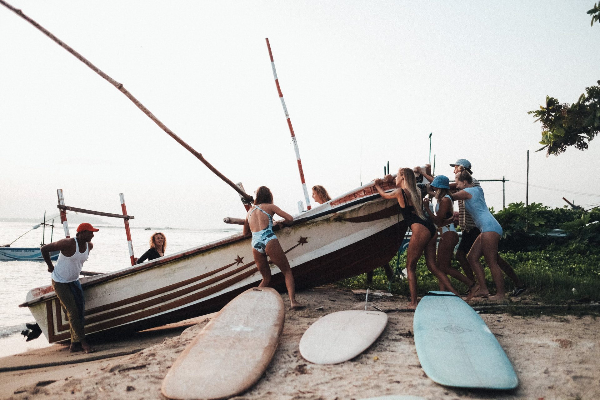 Guests helping push a traditional fishing boat down the beach at sunrise
