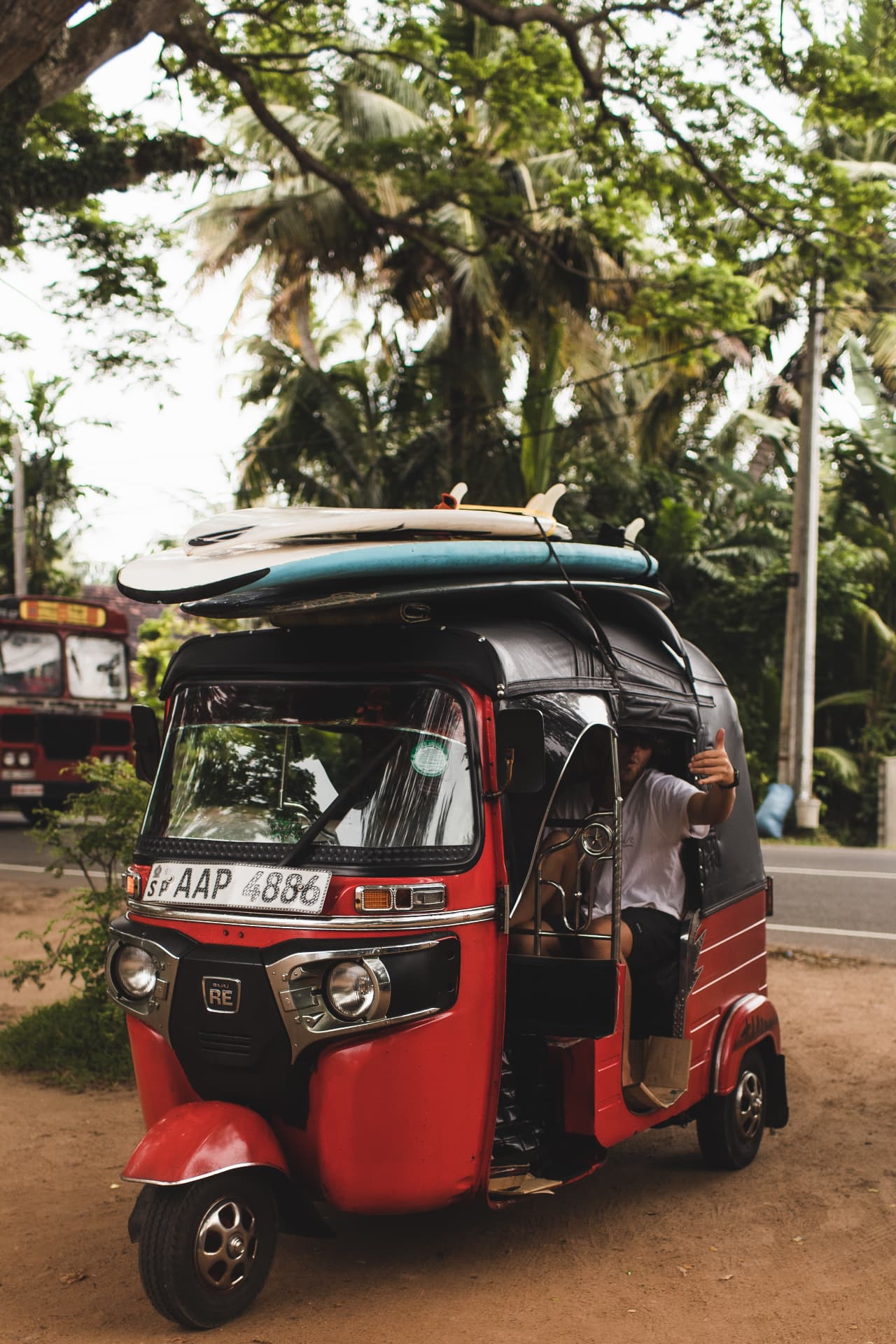 A red tuk-tuk loaded with surfboards under the palms