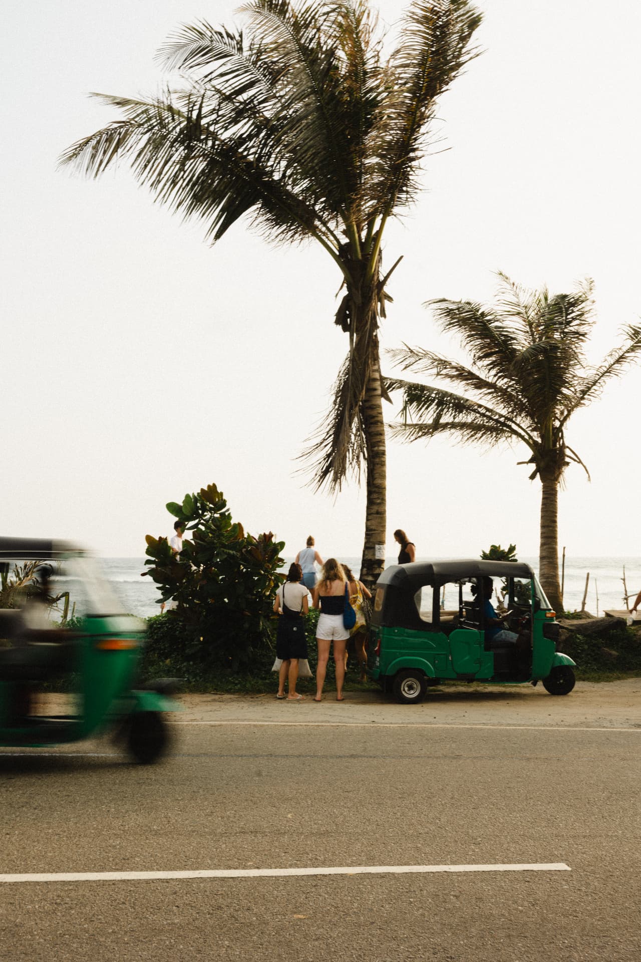 Green tuk-tuks and palm trees along the coast road near the villa