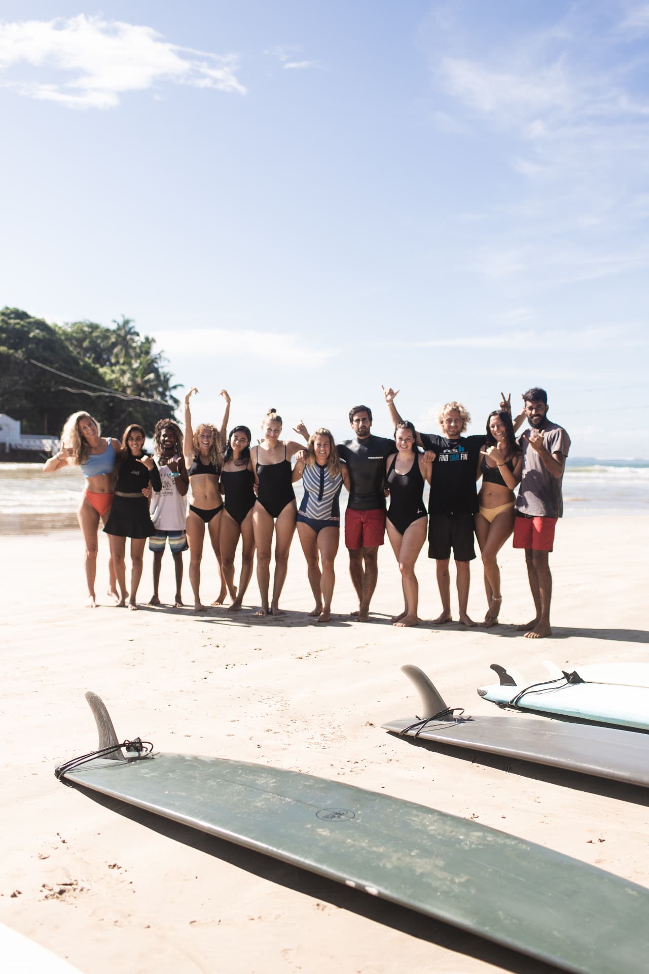 A group of guests lined up on the beach with surfboards