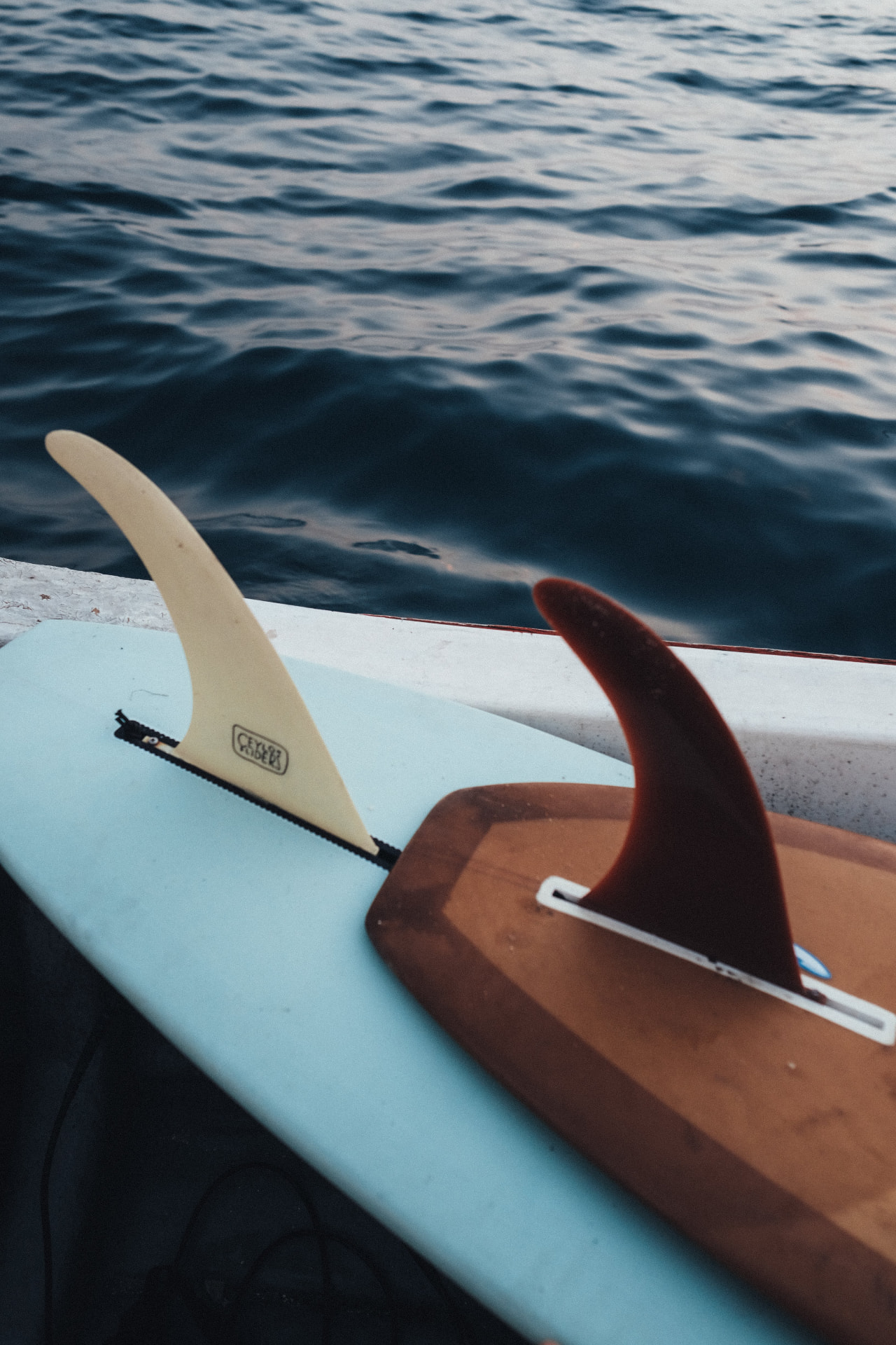 Two longboard fins resting on a boat above dark ocean water