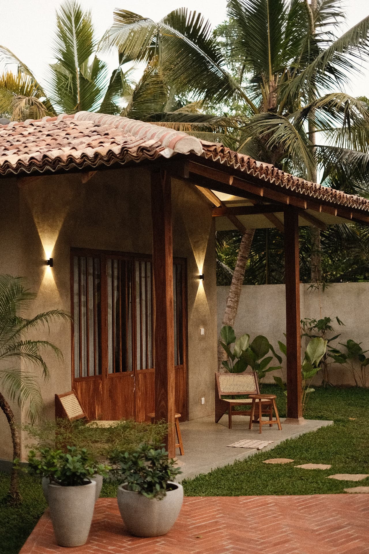 A small tiled-roof bungalow porch lit by warm wall lights at dusk