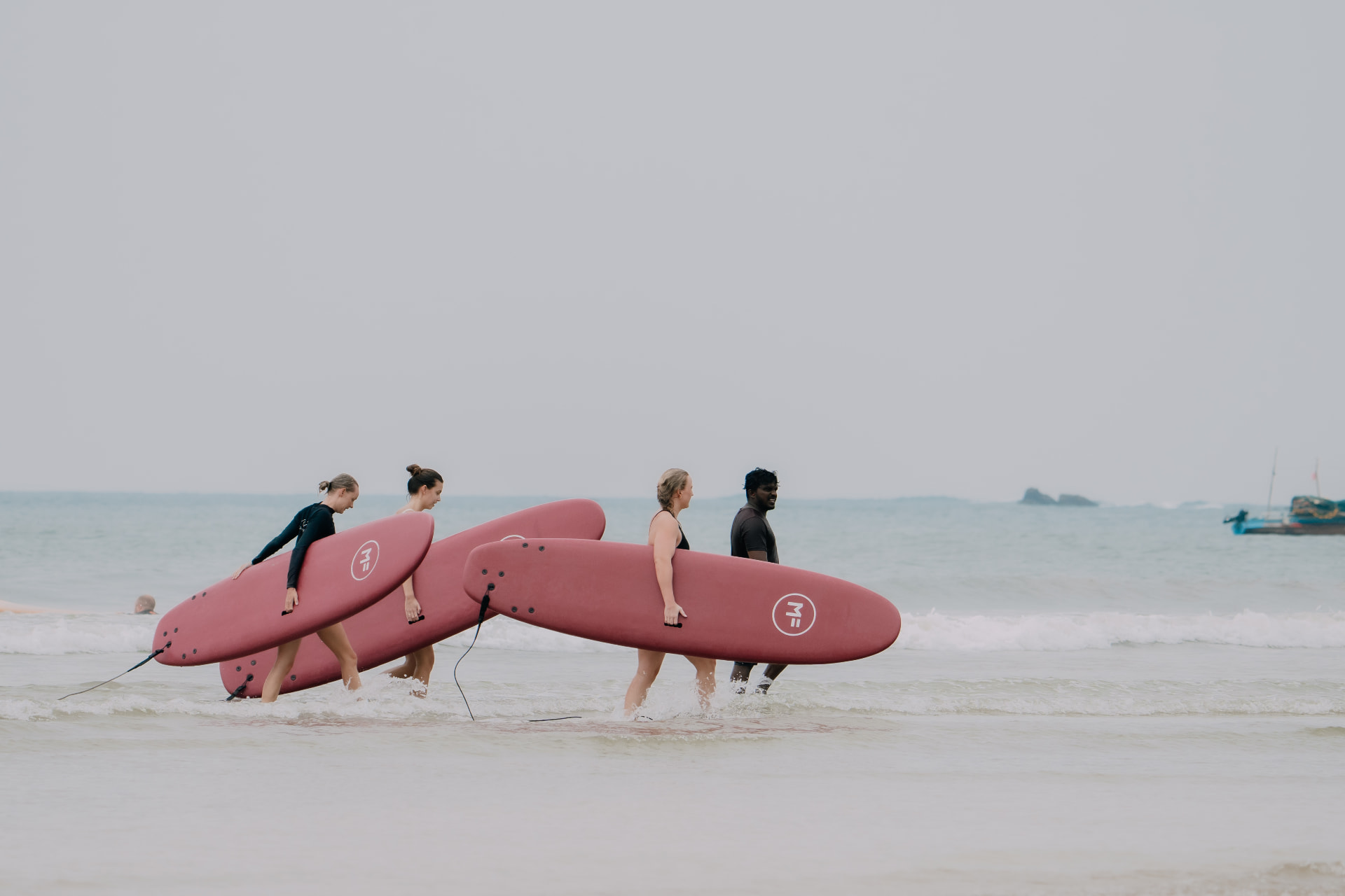 Guests carrying soft-top surfboards into the ocean during a beginner surf lesson in Ahangama