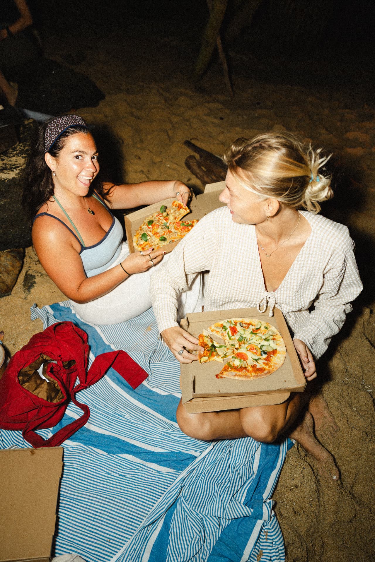 Two guests sharing pizza on the beach at night