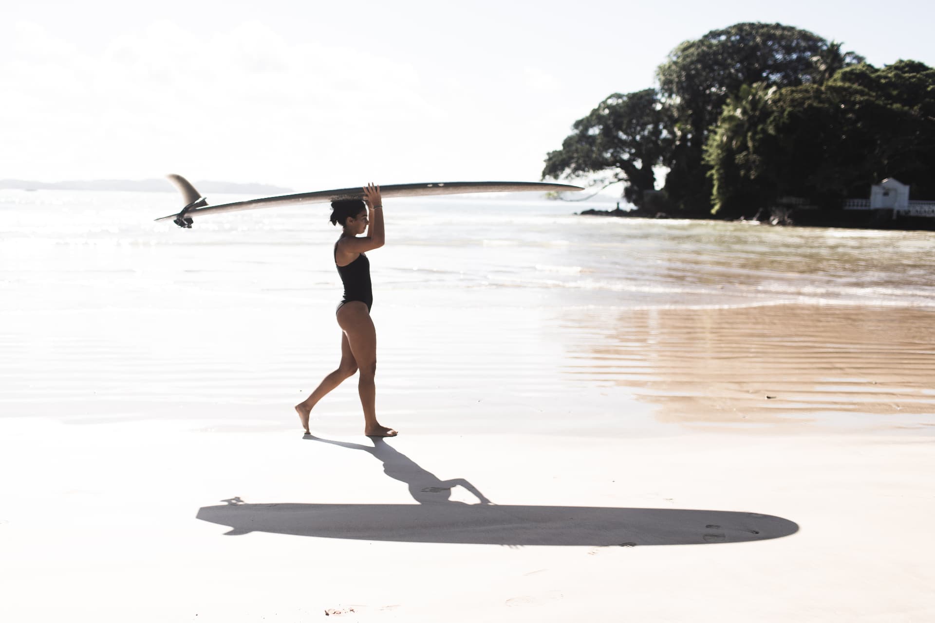 A guest carrying a longboard across the sand
