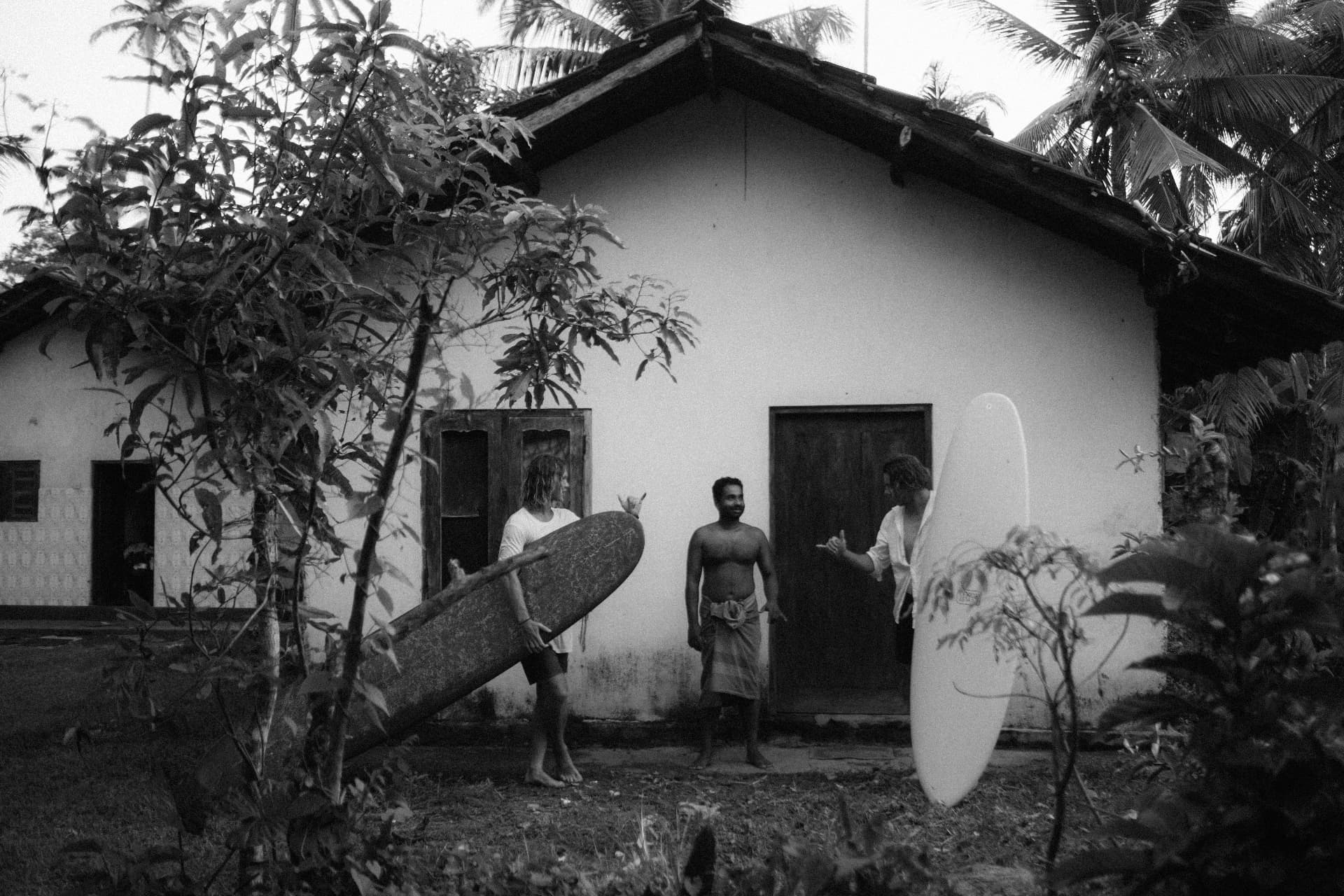 Three friends with surfboards outside a jungle house